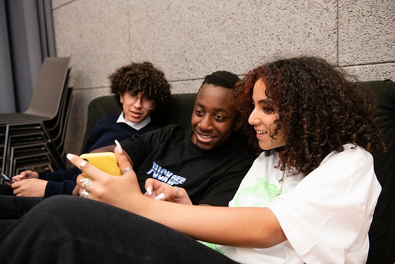 Medienzentrum_c_Liebentritt_112 Drei Jugendliche sitzen auf einem Sofa und schauen gemeinsam auf ein gelbes Handy